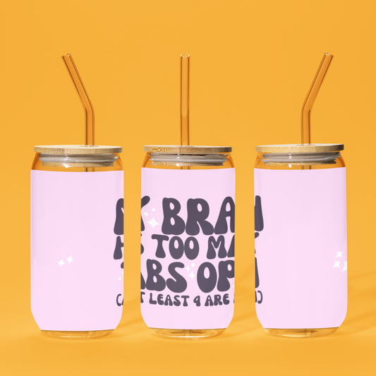 16oz reusable glass tumbler with bamboo lid and straw featuring the humorous quote 'My Brain Has Too Many Tabs Open (And at Least 9 Are Frozen)' in bold, playful typography on a pastel pink background. Perfect for multitaskers with a sense of humor.