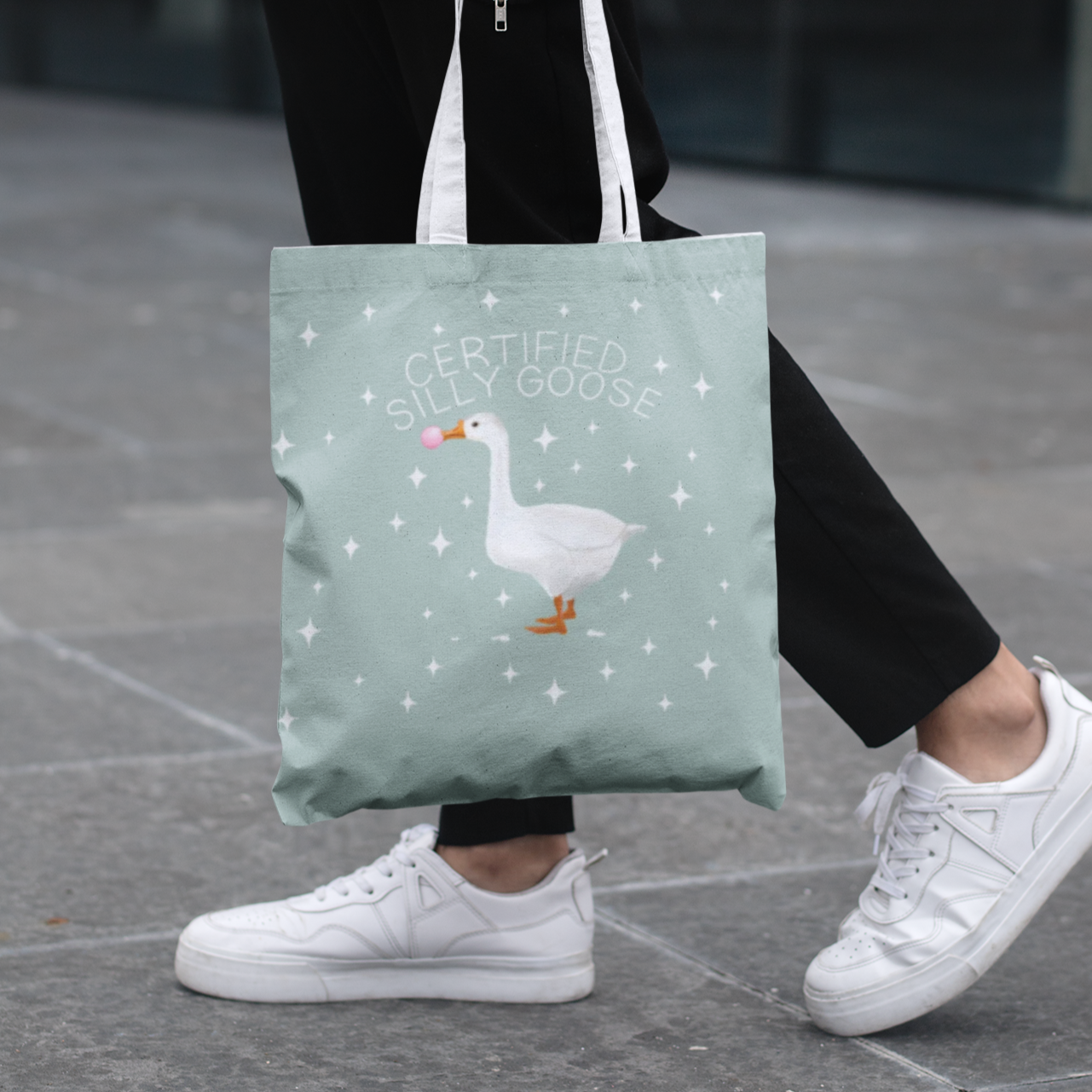 Person holding a tote bag with a goose design on a pavement