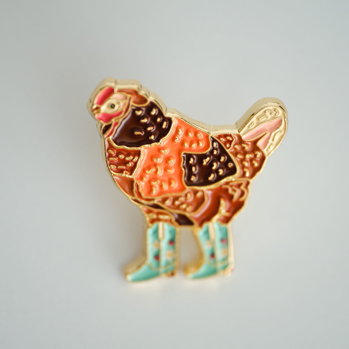 Cowgirl Chicken enamel pin with a chicken in mint strawberry-patterned boots.