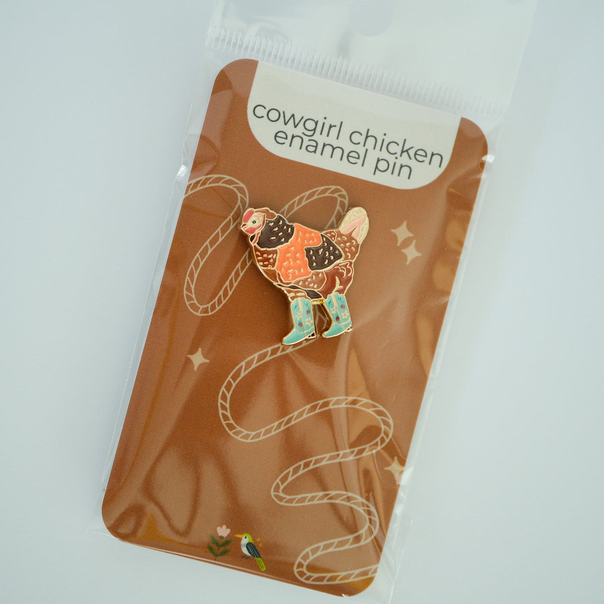 Cowgirl Chicken enamel pin with a chicken in mint strawberry-patterned boots on its product backing card.
