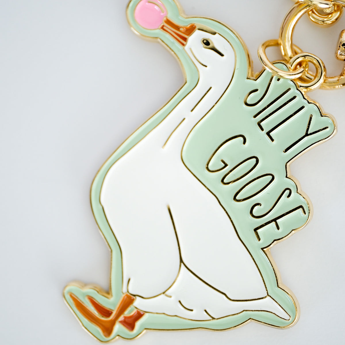 Close-up of silly Goose keychain featuring a white goose blowing pink bubblegum, with mint enamel and gold hardware.