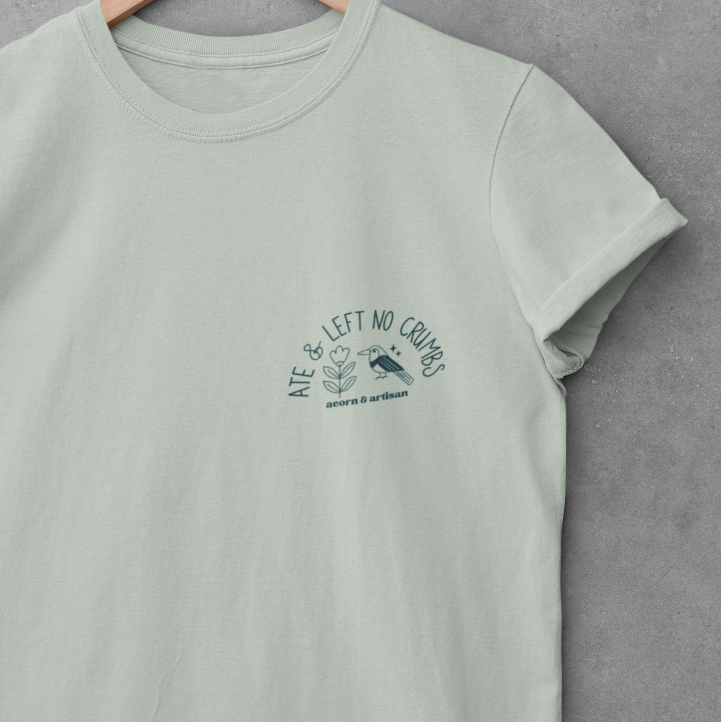 Mint green t-shirt with a graphic design on a hanger against a gray background