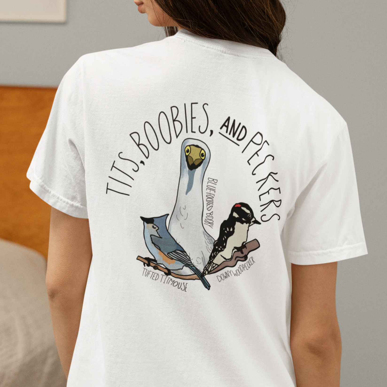 Person wearing a white t-shirt with graphic design and text in a bedroom setting