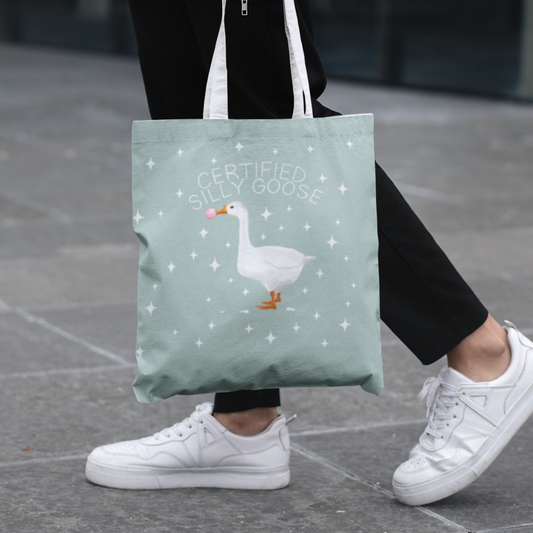 Person holding a tote bag with a goose design on a pavement