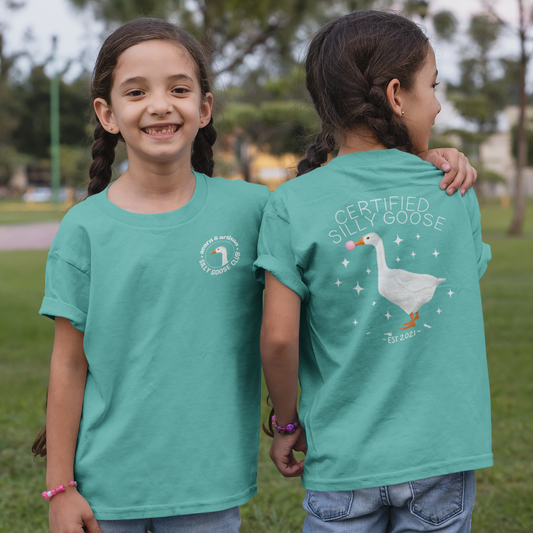 Two children wearing teal t-shirts with a duck graphic and text in an outdoor setting.