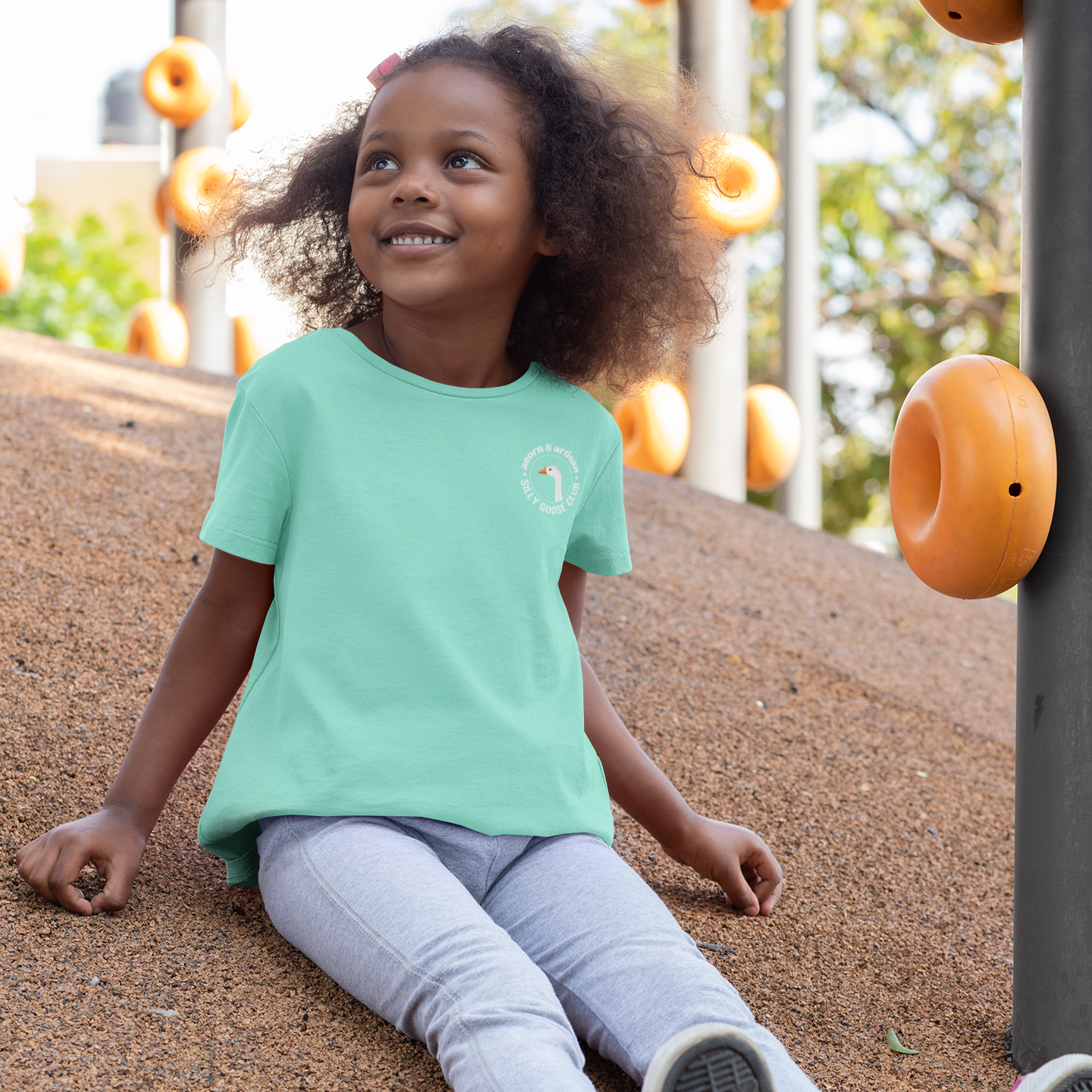 Child sitting on a playground with a green shirt and gray pants
