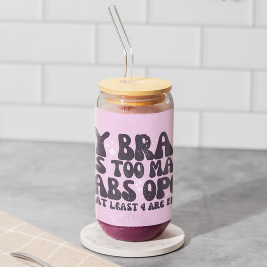 16oz reusable glass tumbler with bamboo lid and straw featuring the humorous quote 'My Brain Has Too Many Tabs Open (And at Least 9 Are Frozen)' in bold, playful typography on a pastel pink background. Perfect for multitaskers with a sense of humor.