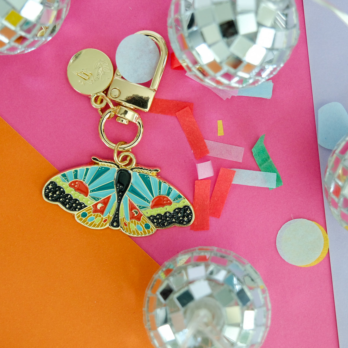 Cosmic Moth Enamel Keychain styled in a colorful lifestyle setting