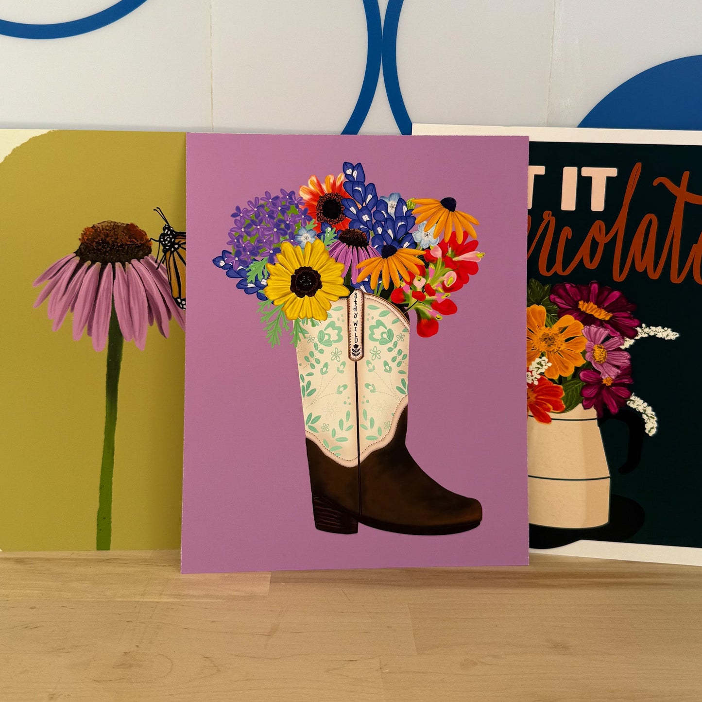 Three art prints with floral designs on a wooden surface.